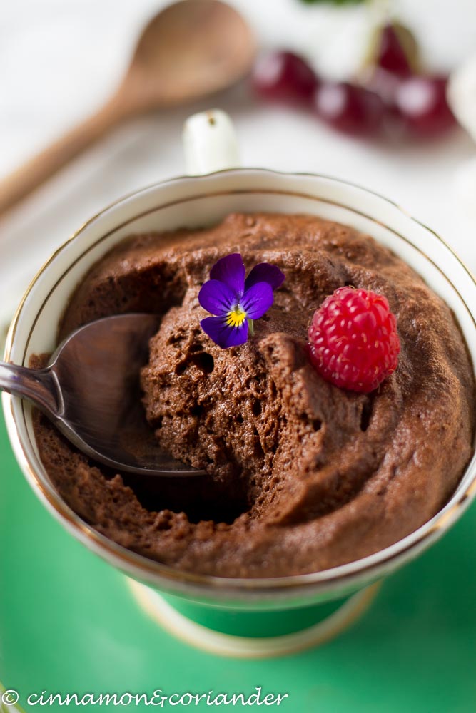 close-up of a spoon being inserted into a fluffy vegan chocolate mousse topped with a raspberry