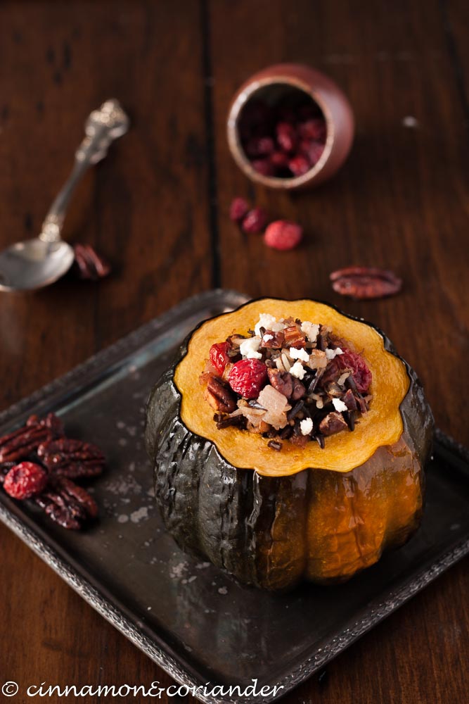 Vegetarian Stuffed Acorn Squash with wild rice, cherries, pecans and crumbled cheese on silver platter with a small dish with dried fruit in the background