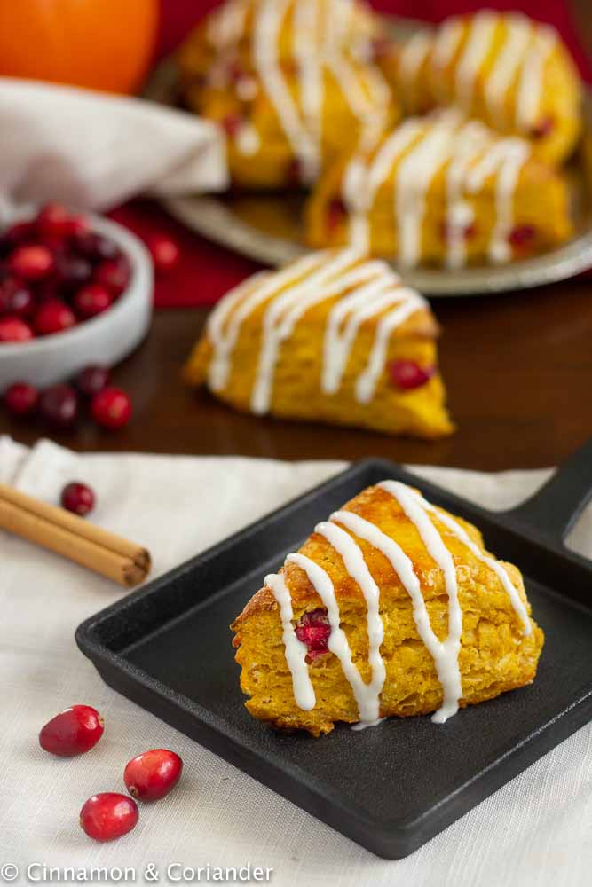 Starbucks Copycat Cranberry Pumpkin Scones glazed with Cream Cheese Icing on a rustic black plate with fresh cranberries in the background