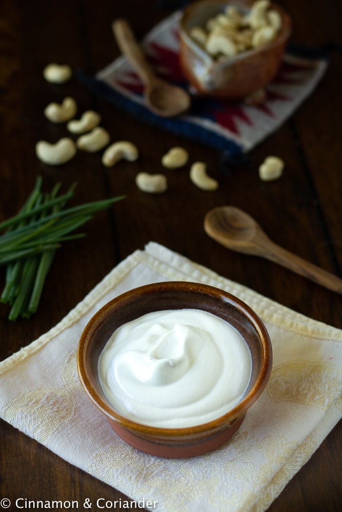 easy vegan sour cream in a rustic ceramic dish with cashews and chives in the background