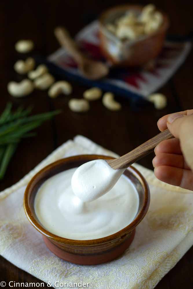 Homemade vegan sour cream in a small bowl with chives and cashews in the background