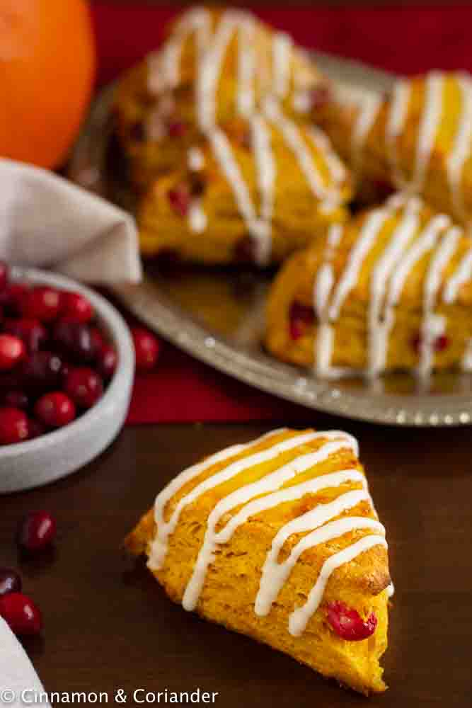 Starbucks Copycat Cranberry Pumpkin Scones with Cream Cheese Icing arranged on a wooden table with a pumpkin and cranberries 