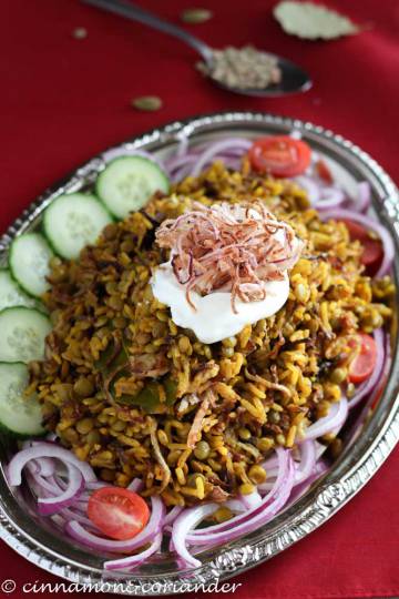 Mejadra Arabic Lentil Rice Pilaf on a silver platter with sliced cucumbers on the side and fried onions on top