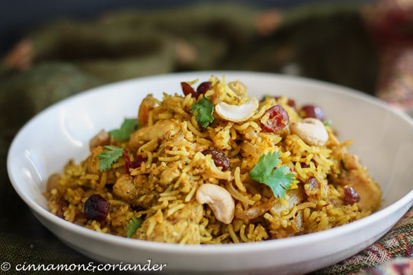 a serving of homemade chicken biryani sprinkled with dried fruit, nuts and cilantro