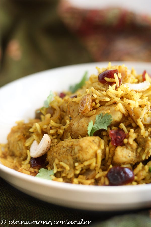 Einfache indische Reispfanne mit Hähnchen, Nüssen und Rosinen in einer Schale mit frischem Koriander angerichtet