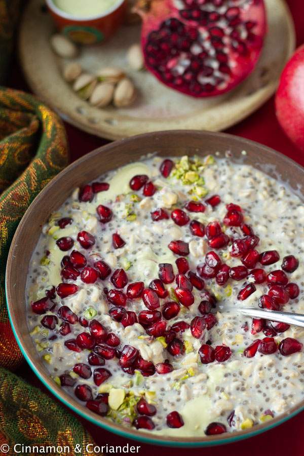 a spoon stirring a bowl of vegan clean eating overnight oats with pistachios and pomegranate seeds