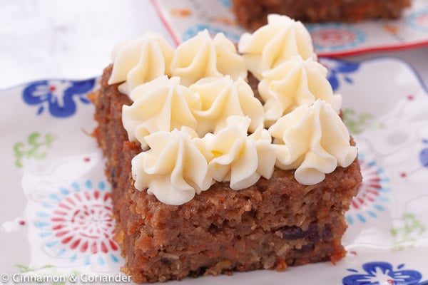 a slice of carrot cake with piped cream cheese frosting on a plate