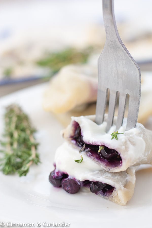 a fork stabbing a homemade Polish blueberry pierogi on a white plate