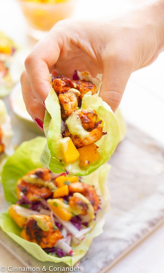 a hand holding a healthy chipotle shrimp lettuce wraps with mango and cilantro sauce