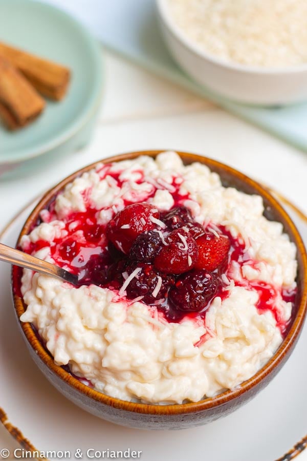 Close-up of a bowl of vegan instant pot rice pudding topped with berries and coconut
