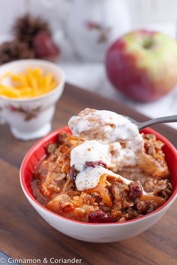 a spoon of the best ever apple crisp with cheddar oat crumble topping served with sour cream
