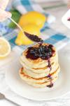 homemade blueberry syrup being drizzled on stack of fluffy pancakes