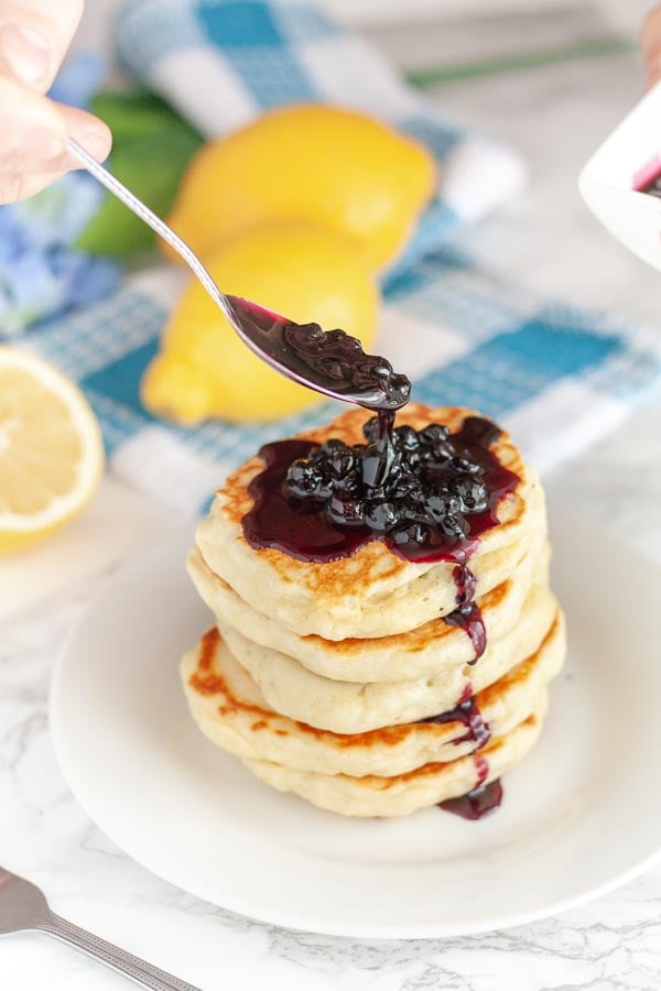 homemade blueberry syrup being drizzled on stack of fluffy pancakes