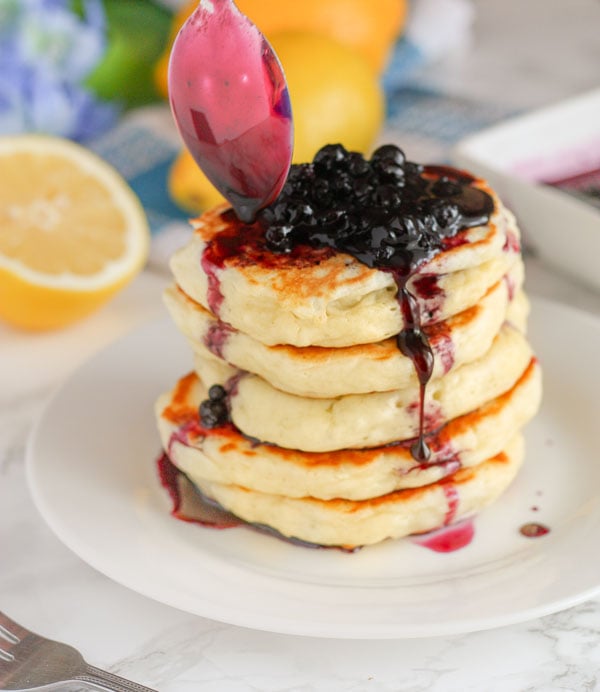 homemade blueberry syrup being drizzled over a stack of fluffy pancakes