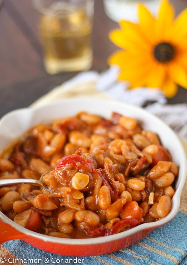 a spoon stirring in a skillet with homemade Maple Molasses Baked Beans with Bacon