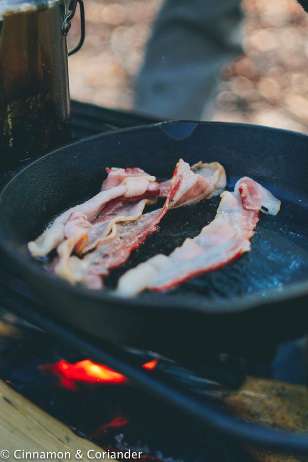 bacon slices frying in a black cast iron skillet