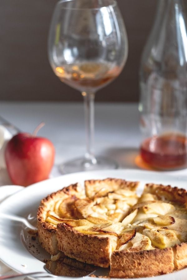 side view of a homemade rustic apple tart with a pitcher of apple cider in the background