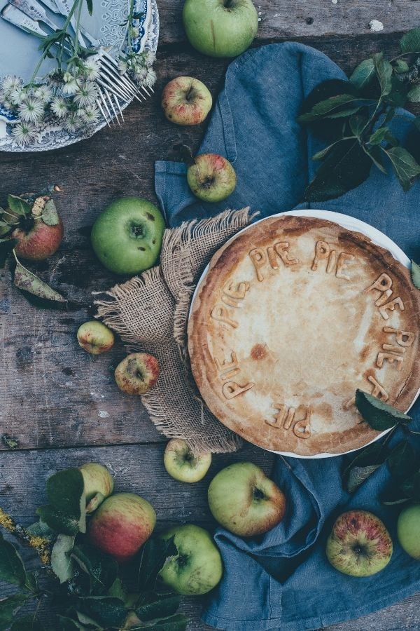overhead shot of a homemade apple pie with a variety of apples surrounding the pie
