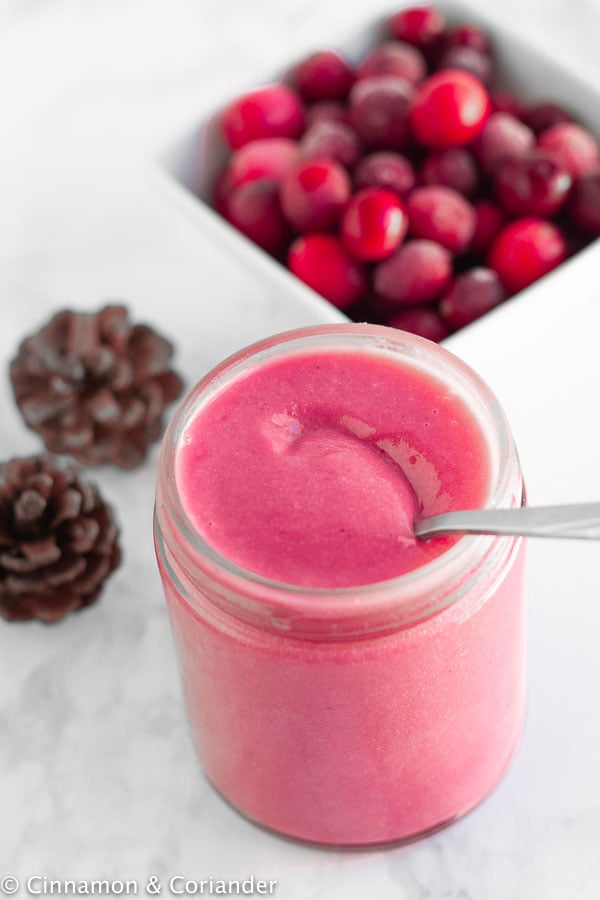 overhead shot of a small glass jar with refined sugar-free cranberry curd with fresh cranberries in the background