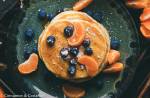 vegane pancakes pfannkuchen auf einem dunklen Teller mit Blaubeeren und Mandarinensirup