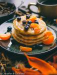 side view of a stack vegan pancakes with almond milk topped with tangerines and blueberries