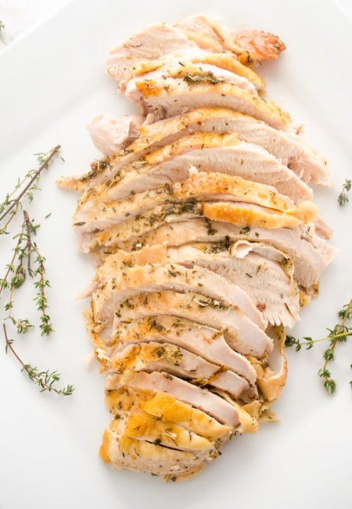 overhead shot of a simple sliced herb and garlic roasted turkey breast on a white platter