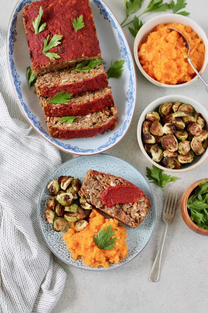 overhead shot of a sliced glazed vegan lentil loaf on a blue platter served with healthy thanksgiving sides 