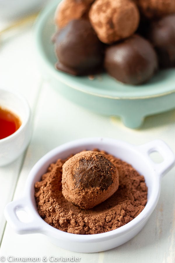 easy healthy rum ball being rolled in a small white dish with organic cocoa powder