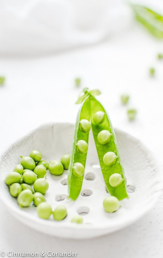 a pod with fresh peas in a white bowl