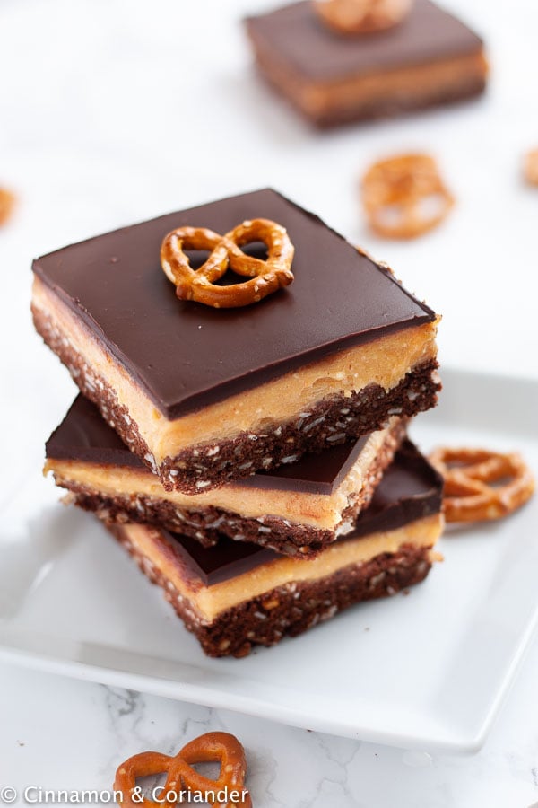 a overhead shot of a stack of Peanut Butter Nanaimo Bars on a white plate with a pretzel on top