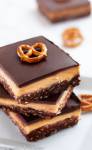 peanut butter Nanaimo bars with pretzel crust stacked on a white plate