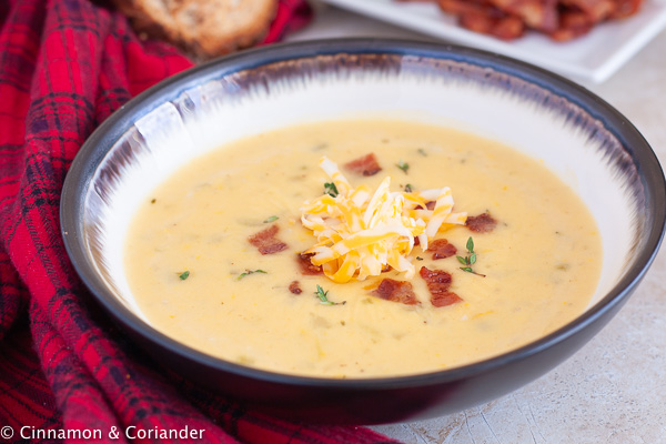 a bowl of beer and cheddar cheese soup topped with grated cheese and bacon