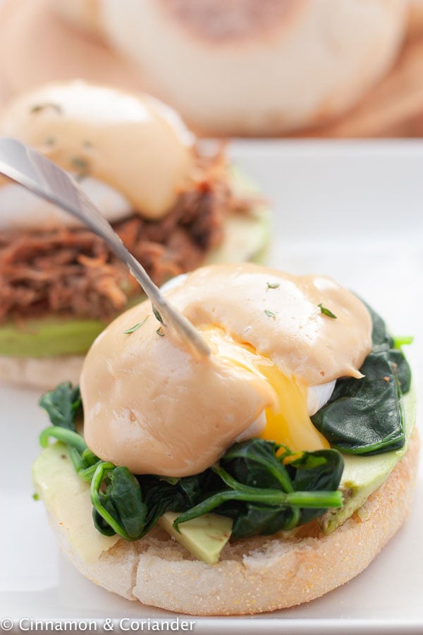 a fork being pierced into the runny egg yolk of a poached eggs Benedict topped with homemade hollandaise sauce