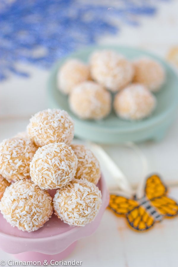 no bake passionfruit cheesecake bites rolled in shredded coconut on a pink cake stand