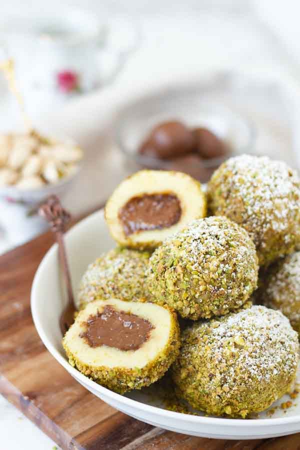 a plate of sweet Nutella Stuffed Semolina Dumplings coated with ground pistachios with truffles in the background