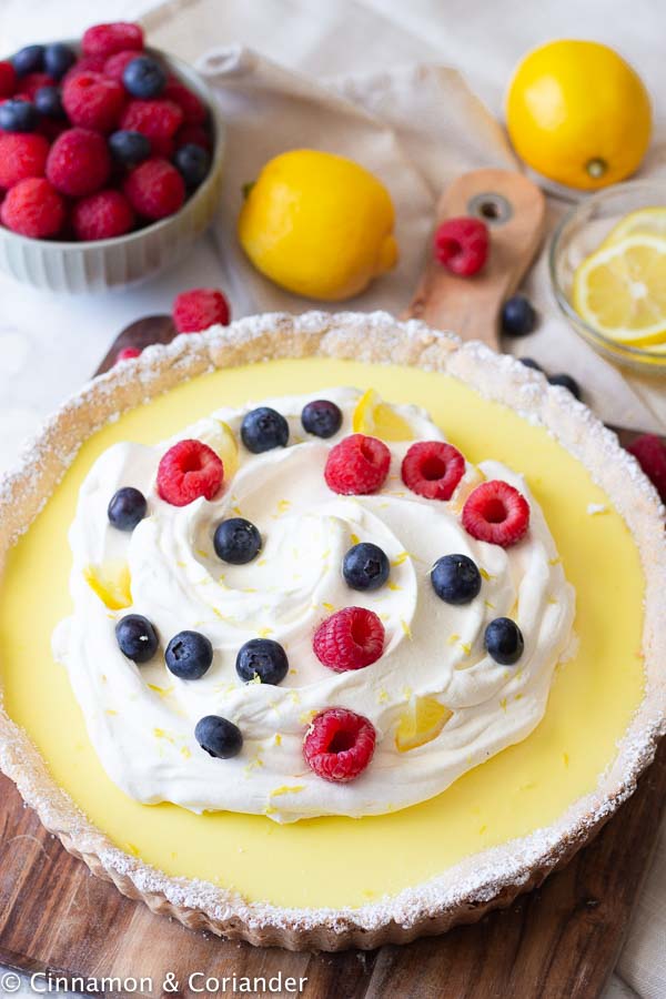 side view of a classic French lemon tart (tarte au citron) topped with whipped cream and berries