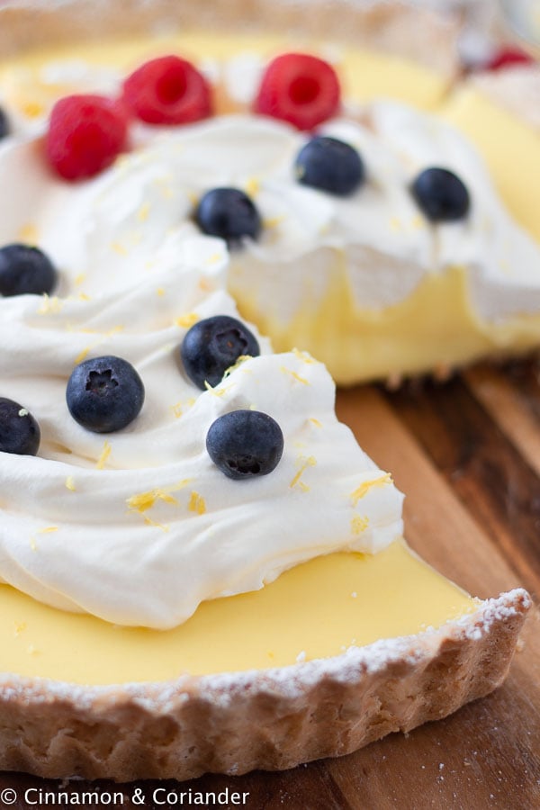 side view of a classic French lemon tart topped with cream and blueberries with one slice cut out