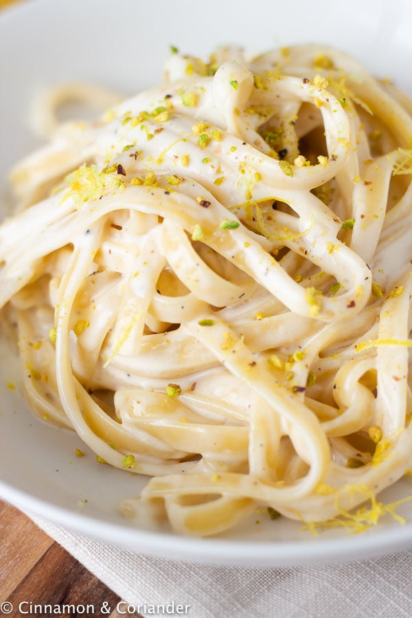close-up side view of a plate of lemon cream pasta sprinkled with chopped pistachios 