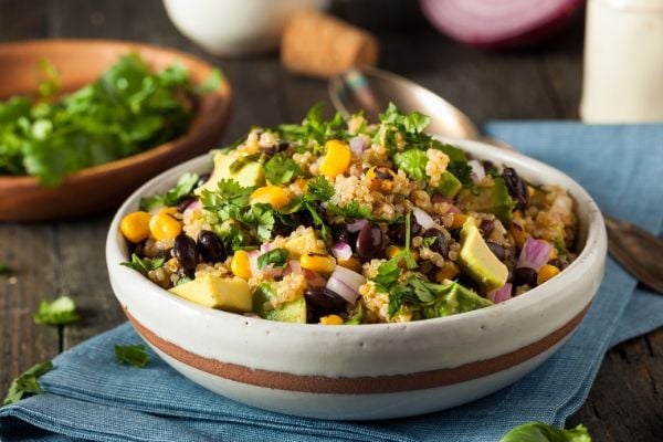 a clay bowl filled with warm quinoa salad with charred corn, black beans, avocado and cilantro lime dressing 