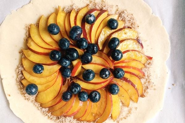 rolled out galette pastry being topped with ground nuts, nectarine slices and blueberries