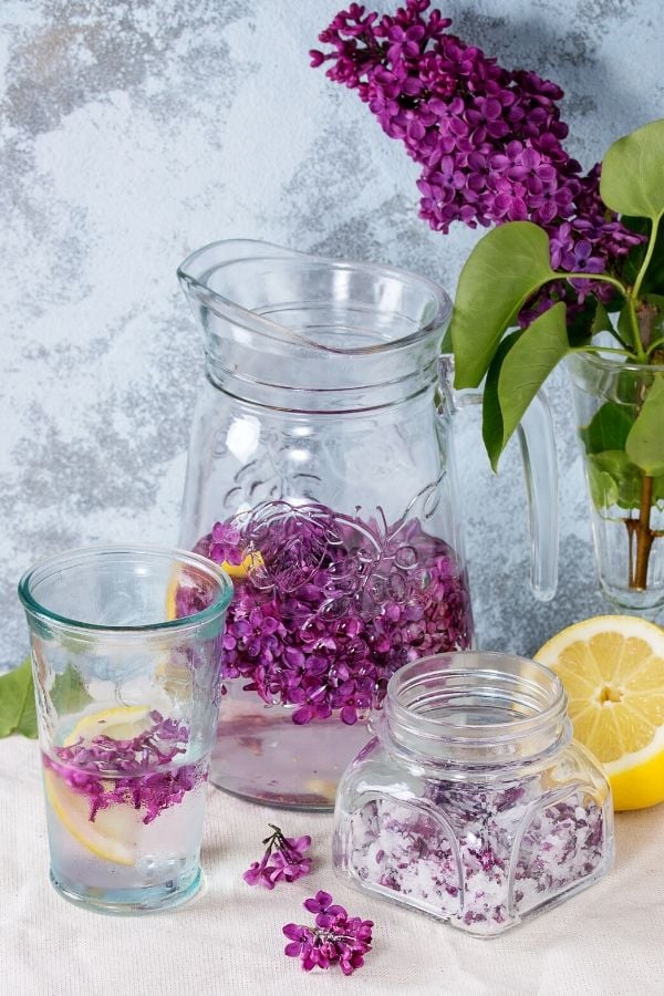 a jar of lilac petal sugar next to a a glass of homemade lilac lemonade 
