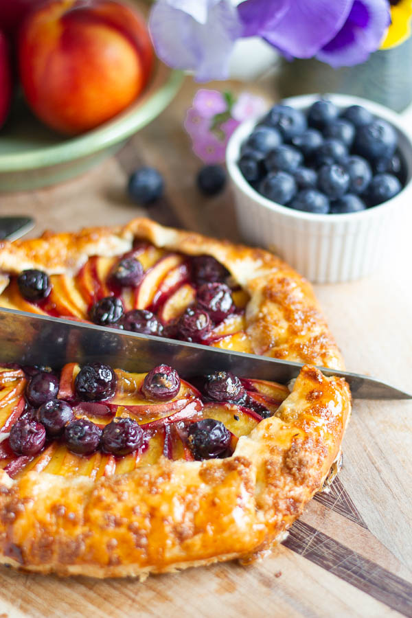 a rustic French Nectarine Blueberry Galette being cut into wedges with a cake knife