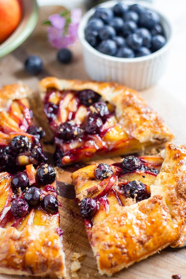 side view of a rustic French Nectarine Blueberry Galette with berries in the background