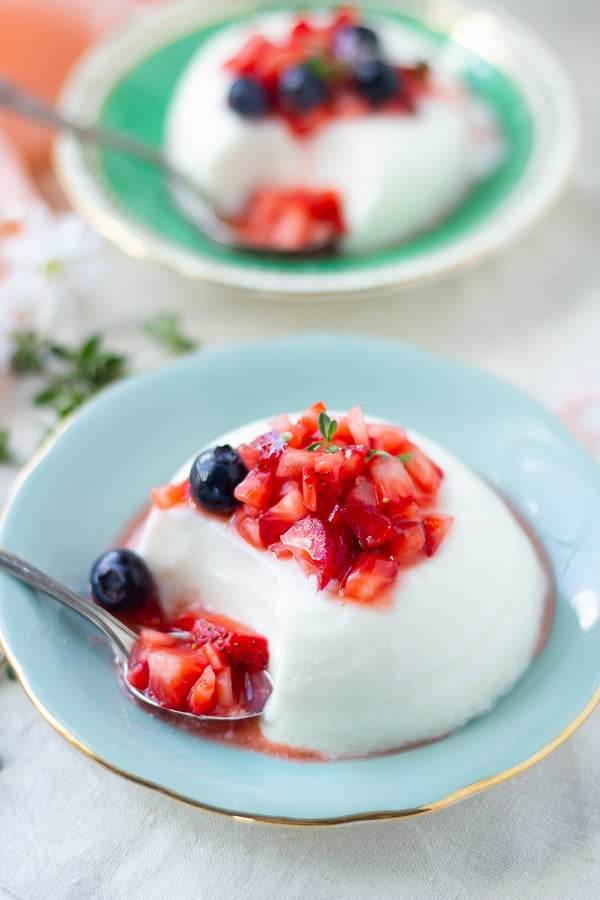 Greek Yogurt panna cotta topped with macerated berries on a pale blue saucer