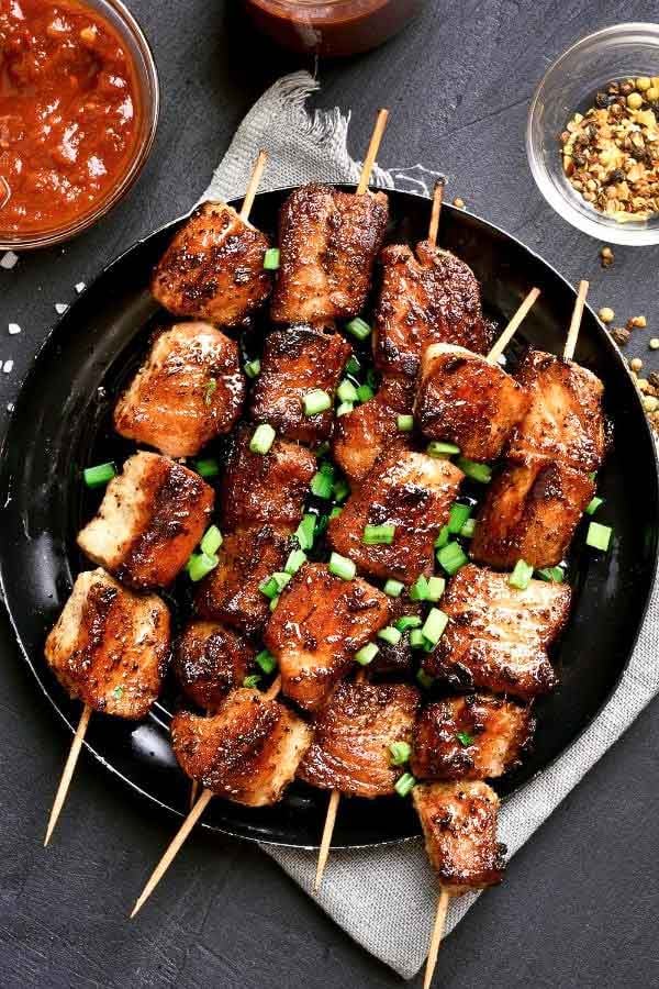 grilled paleo pork satay on a black plate next to bowl with satay dipping sauce