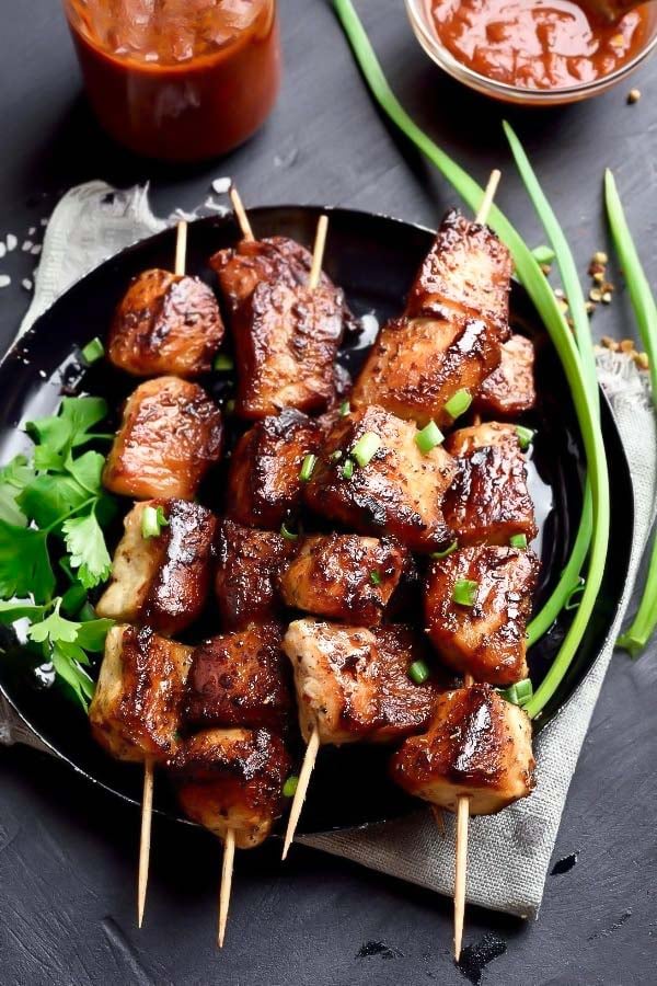 Asian grilled pork shoulder satay skewers on a black plate