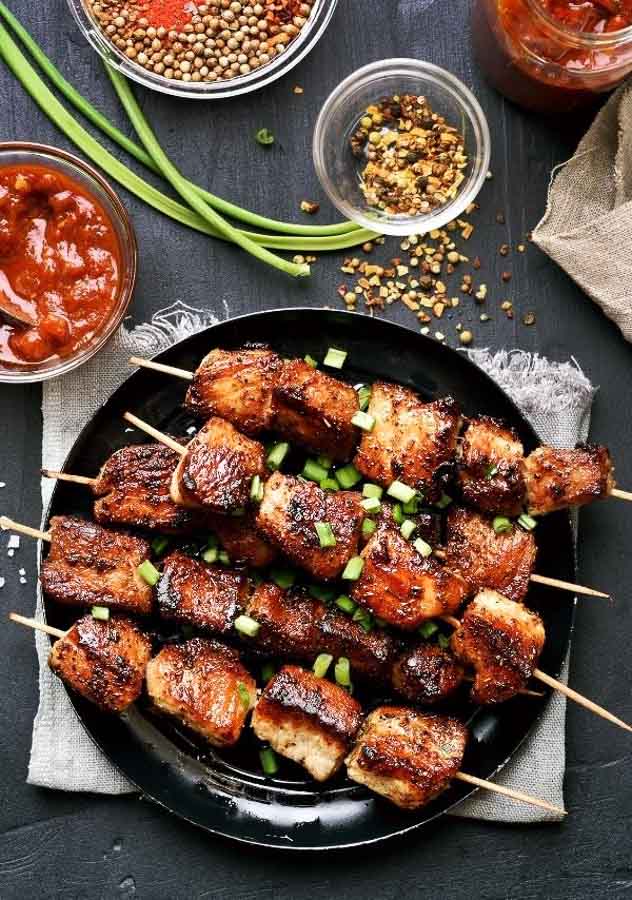 Asian grilled pork shoulder satay skewers surrounded by ground spices and satay sauce