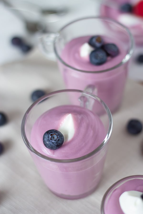 overhead shot of two no bake vegan cheesecake mousse jars topped with coconut whip and blueberries