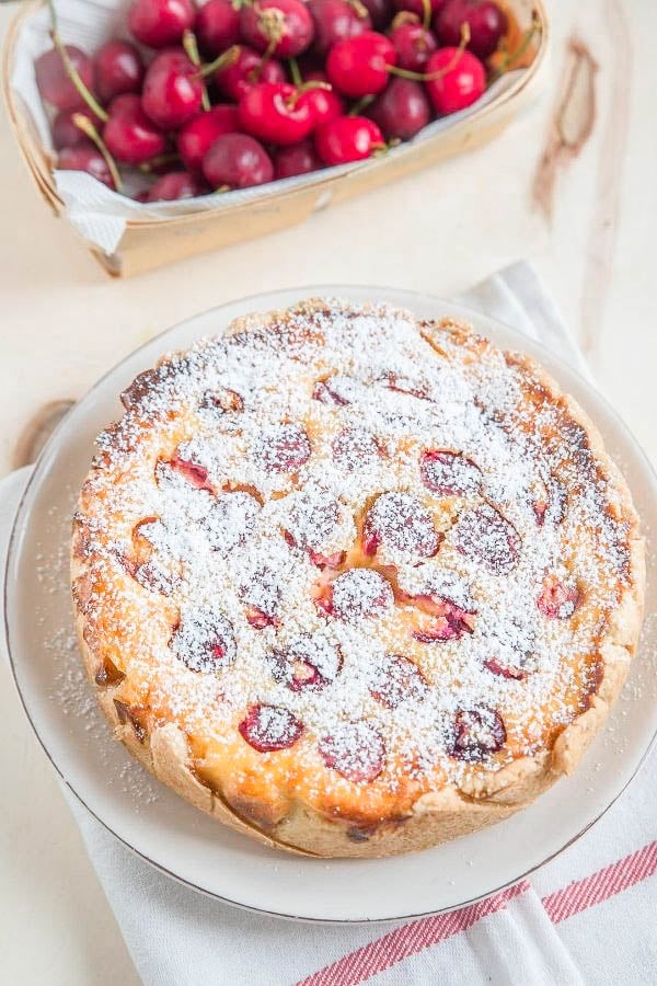 overhead shot of a German cherry custard pie on a cake platter with sour cherries in the background
