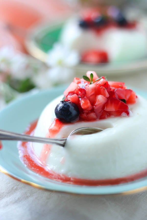 a spoon digging into a Greek yogurt panna cotta topped with macerated berries 